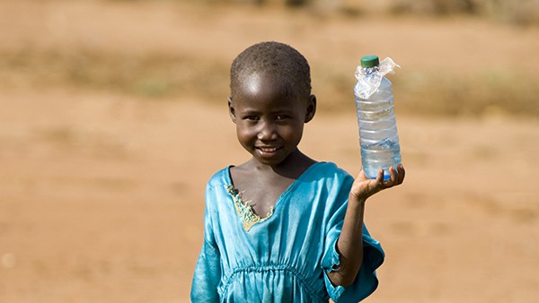 young child transporting an old plastic bottle full of water