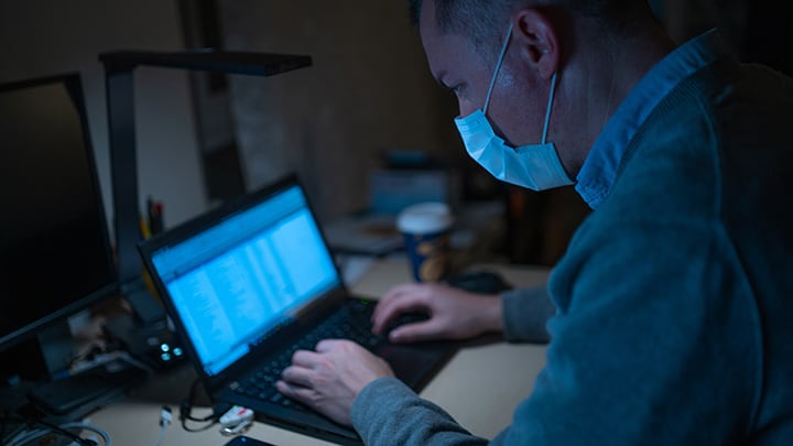 Man in medical mask works on laptop