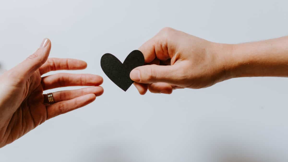 One hand giving a paper heart to another hand