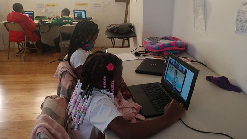 Two girls sitting a table with their laptops engaged in virtually learning at at Ekklesia's learning pod.